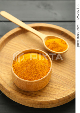 Turmeric (Curcuma) powder on wooden plate on black background 125207190