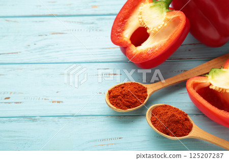 Powder paprika on wooden spoon with fresh red pepper on blue wooden background 125207287