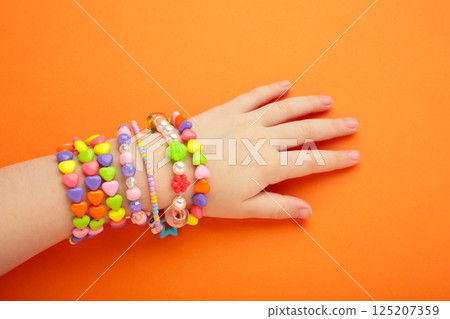 Child wears bracelets on his hands. Kids handmade beaded jewelry on orange background. Child wears bracelets on his hands. Kids handmade beaded jewelry on orange background. 125207359