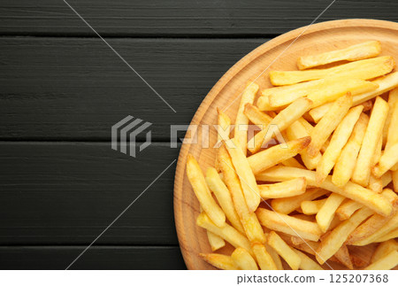 French fries on wooden cutting board on black wooden background. Top view French fries on wooden cutting board on black wooden background. Top view 125207368