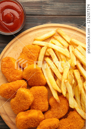Homemade chicken nuggets and french fries with ketchup on brown wooden background. Homemade chicken nuggets and french fries with ketchup on brown wooden background. 125207374