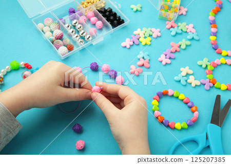 Little girl made bracelets on blue background. Kids handmade beaded jewelry. DIY bracelet beads. 125207385