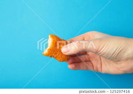 Chicken nugget with a bite taken in hand on a blue background 125207416