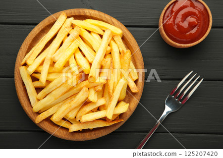 French fries on wooden plate with ketchup in bowl on black wooden background. 125207420
