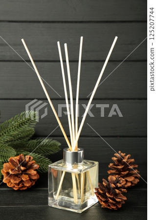 Glass bottle of aroma diffuser and pine cones on black wooden background. Vertical photo Glass bottle of aroma diffuser and pine cones on black wooden background. Vertical photo 125207744