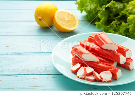Tasty crab sticks, pieces of lemon and salad on plate on blue background. Tasty crab sticks, pieces of lemon and salad on plate on blue background. 125207745