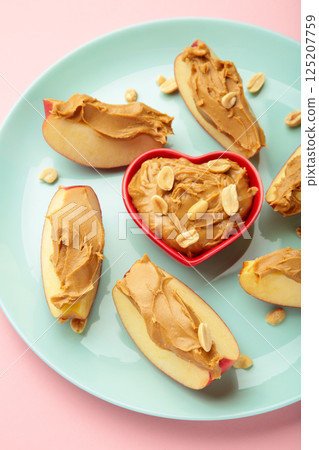 Slices of fresh apple with peanut butter in bowl on mint plate on pink background. Vertical photo 125207759