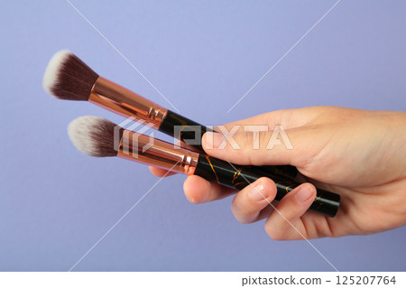 Female hand with make-up artist brush on purple background 125207764