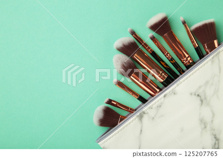 Cosmetic bag with different brushes of professional makeup artist on mint background Cosmetic bag with different brushes of professional makeup artist on mint background 125207765