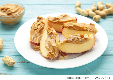 Slices of fresh apple with peanut butter on plate on blue background. Slices of fresh apple with peanut butter on plate on blue background. 125207823
