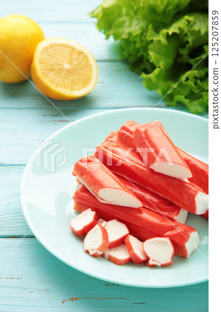 Tasty crab sticks, pieces of lemon and salad on plate on blue background. Tasty crab sticks, pieces of lemon and salad on plate on blue background. 125207859
