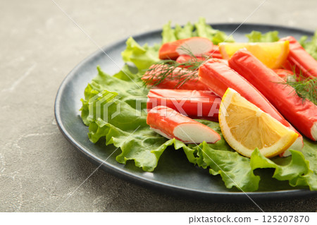 Tasty crab sticks, pieces of lemon and salad on plate on grey background. Tasty crab sticks, pieces of lemon and salad on plate on grey background. 125207870