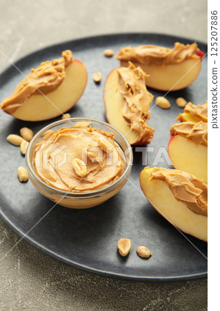 Slices of fresh apple with peanut butter in bowl on blue plate on grey background. Slices of fresh apple with peanut butter in bowl on blue plate on grey background. 125207886