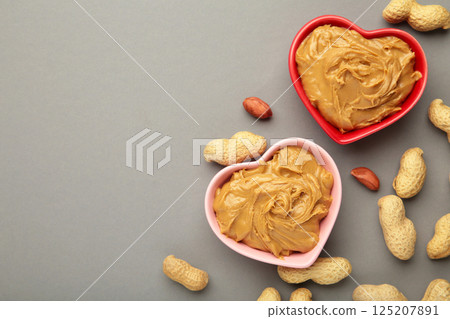 Heart shaped bowl with peanut butter and peanuts on grey background. Creamy peanut pasta in small bowl. 125207891