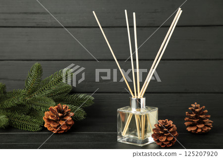 Glass bottle of aroma diffuser and pine cones on black wooden background. 125207920