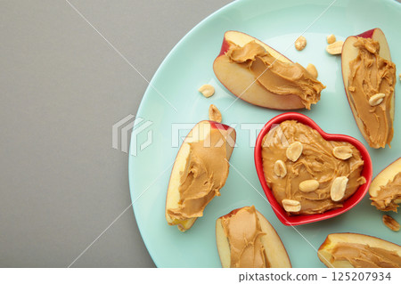 Slices of fresh apple with peanut butter in bowl on mint plate on grey background. Slices of fresh apple with peanut butter in bowl on mint plate on grey background. 125207934