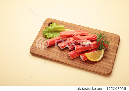 Fresh crab sticks with lemon on cutting board on beige background. Fresh crab sticks with lemon on cutting board on beige background. 125207936