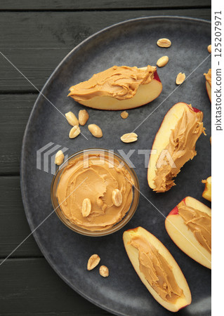 Slices of fresh apple with peanut butter and nuts on dark background. 125207971