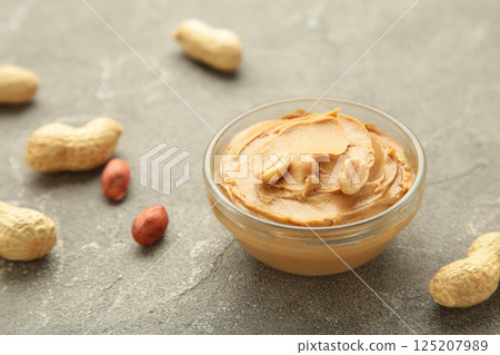 Bowl of peanut butter and peanuts on grey concrete background. Creamy peanut pasta in small bowl. 125207989