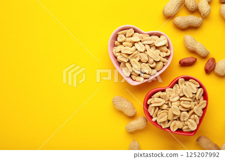 Peanuts in a heart shaped bowl on yellow background. 125207992