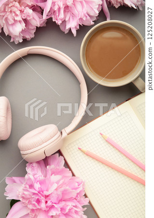 Modern pink headphones with flowers peonies and notebook on grey background. Vertical photo 125208027