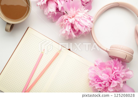 Modern pink headphones with flowers peonies and notebook on light background 125208028
