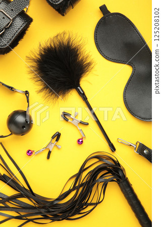 Set of erotic toys for BDSM on yellow background. The game of sexual slavery with a whip, gag and leather blindfold. Intimate sex games. Vertical photo Set of erotic toys for BDSM on yellow background. The game of sexual slavery with a whip, gag and leather blindfold. Intimate sex games. Vertical photo 125208102