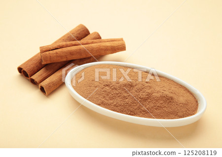 Cinnamon sticks and powder in bowl on beige background. Cinnamon sticks and powder in bowl on beige background. 125208119