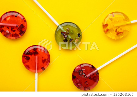 Colorful sweet lollipops with berries on yellow background. Colorful sweet lollipops with berries on yellow background. 125208165