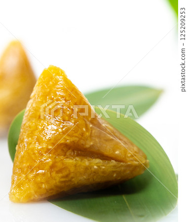 Three golden alkaline rice dumplings are placed on green bamboo leaves 125209253