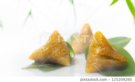 三顆金黃色的鹼粽放置於綠色竹葉上 125209260