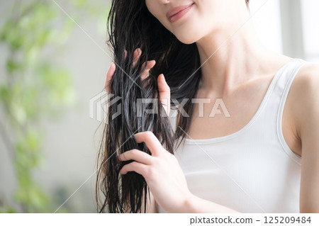 Image of a young woman applying hair oil to her wet hair as a treatment Image of a young woman applying hair oil to her wet hair as a treatment 125209484