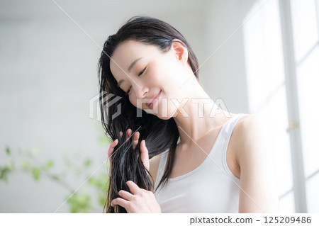 年輕女子在濕髮上塗抹髮油進行護理。圖中顯示了該療法用於治療頭髮分叉和其他頭髮問題。 年輕女子在濕髮上塗抹髮油進行護理。圖中顯示了該療法用於治療頭髮分叉和其他頭髮問題。 125209486