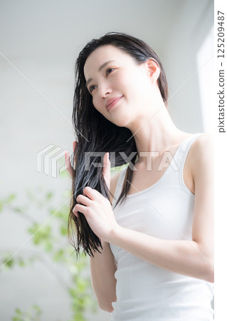 A young woman applies hair oil to her wet hair as a treatment. Image shows the treatment being used to treat split ends and other hair problems. A young woman applies hair oil to her wet hair as a treatment. Image shows the treatment being used to treat split ends and other hair problems. 125209487
