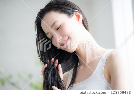 A young woman applies hair oil to her wet hair as a treatment. Image shows the treatment being used to treat split ends and other hair problems. A young woman applies hair oil to her wet hair as a treatment. Image shows the treatment being used to treat split ends and other hair problems. 125209488
