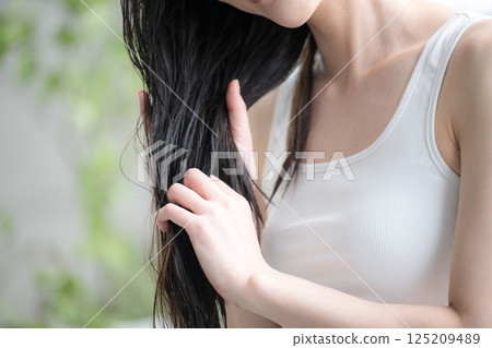 Image of a young woman applying hair oil to wet hair as a treatment. No face, taking care of split ends at the ends of the hair. Image of a young woman applying hair oil to wet hair as a treatment. No face, taking care of split ends at the ends of the hair. 125209489