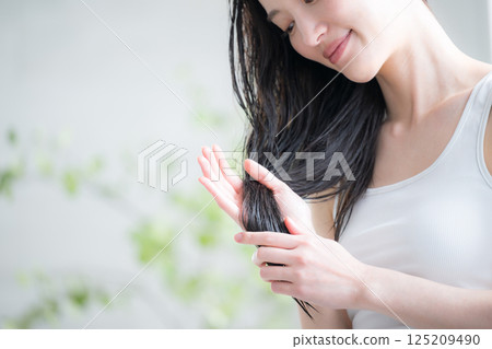 Image of a young woman applying hair oil to wet hair as a treatment. No face, taking care of split ends at the ends of the hair. 125209490