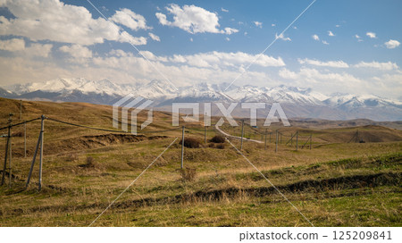 Panoramic mountain landscape with winding road through vast steppe and snow capped peaks 125209841