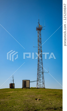 Telecommunications tower on hilltop with equipment cabins against clear blue sky 125209847