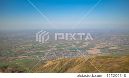 Aerial panoramic view of agricultural landscape with foothills and distant settlements under clear blue sky 125209848