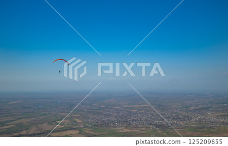 Paraglider with orange wing soaring against clear blue sky Paraglider with orange wing soaring against clear blue sky 125209855