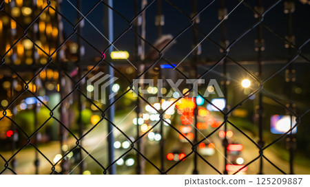 Urban Night Cityscape Through Chain Link Fence with Colorful Bokeh Lights from Traffic and Buildings 125209887