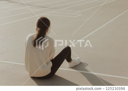 Woman sitting alone on sunlit track, contemplating in casual attire 125210398