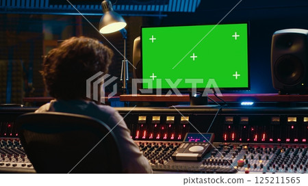 Sound designer watches online tutorials via greenscreen monitor to mix and master tracks and create music for his album. Audio engineer producing songs by twisting knobs and pushing faders. Camera A. 125211565