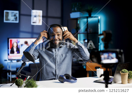 African american man filming himself listening to new album from favorite artist, reviewing music. Online influencer rating songs after hearing them through noise cancelling headphones African american man filming himself listening to new album from favorite artist, reviewing music. Online influencer rating songs after hearing them through noise cancelling headphones 125211627