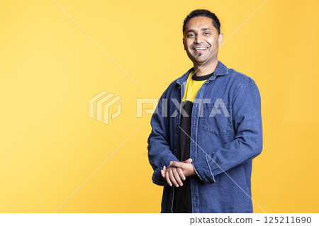Portrait of jolly indian man smiling and posing with arms crossed standing against studio background. Joyous upbeat male person in casual clothing showcases positive emotions. 125211690
