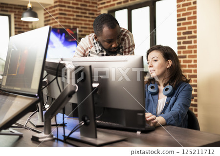 African american man standing and discussing with caucasian woman at desk, analyzing product designs on computer. Diverse employees cooperate in preparing creative projects in brick wall office. African american man standing and discussing with caucasian woman at desk, analyzing product designs on computer. Diverse employees cooperate in preparing creative projects in brick wall office. 125211712