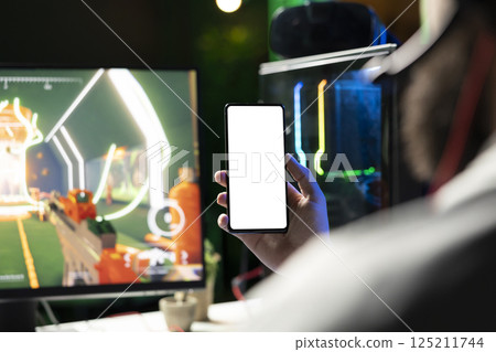 Man looking at mockup phone while playing SF FPS videogame, having fun in dark apartment room. Gamer holding isolated screen smartphone, competing in PvP internet multiplayer game, close up Man looking at mockup phone while playing SF FPS videogame, having fun in dark apartment room. Gamer holding isolated screen smartphone, competing in PvP internet multiplayer game, close up 125211744