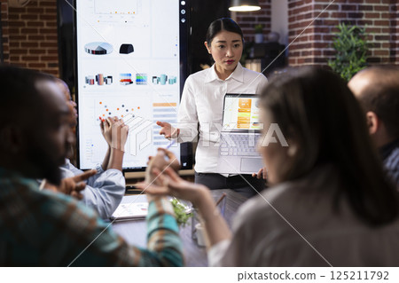 Female entrepreneur discusses financial planning with employees, using laptop to display business analytics. The evening meeting highlights readiness, strategy and deadline driven decision making. Female entrepreneur discusses financial planning with employees, using laptop to display business analytics. The evening meeting highlights readiness, strategy and deadline driven decision making. 125211792