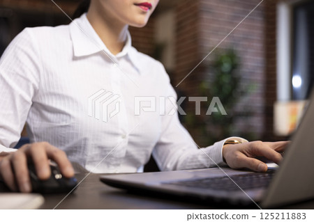 Asian female professional typing diligently on her laptop at her office desk. The closeup shot emphasizes her fingers, showing her focus on data analysis and business reporting in modern workspace. 125211883